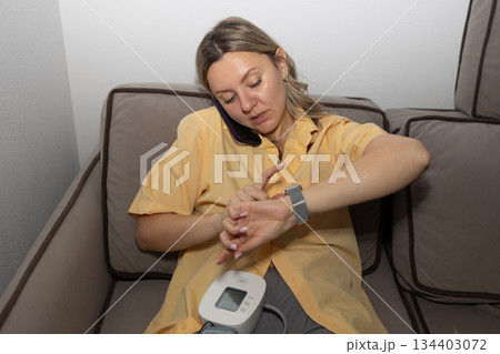 Woman Checks Time While Talking on Phone and Monitoring Blood Pressure at Home Woman Checks Time While Talking on Phone and Monitoring Blood Pressure at Home 134403072