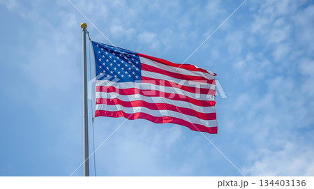 American Flag Flown On Tall Flagpole Against Clear Blue Sky, Symbol Of Freedom And Patriotism 134403136