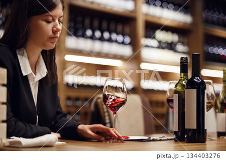 Female sommelier swirling red wine in glass on cellar background being in cellar. Wine expert exam to study different wine.  134403276