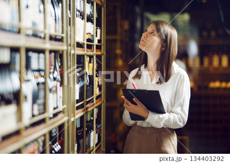 Professional female sommelier making notes on tablet being in wine cellar. Winemaking school and tasting alcoholic beverages. 134403292