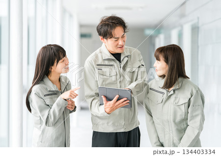タブレットを見ながら会話する作業着・作業衣服を着た製造業・建築業・運送業・建設業の男女スタッフ タブレットを見ながら会話する作業着・作業衣服を着た製造業・建築業・運送業・建設業の男女スタッフ 134403334