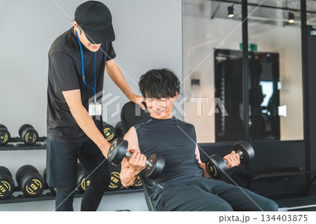 フィットネスジムでダンベルトレーニングを男性とトレーナーの男性スタッフ 134403875
