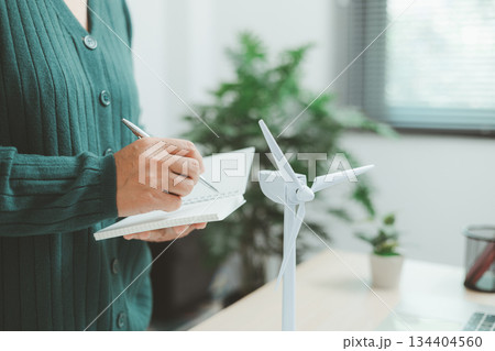 Eco-friendly office scene with person working on laptop near solar panel and wind turbine model, representing green business, renewable energy innovation and sustainable technology workspace. Eco-friendly office scene with person working on laptop near solar panel and wind turbine model, representing green business, renewable energy innovation and sustainable technology workspace. 134404560