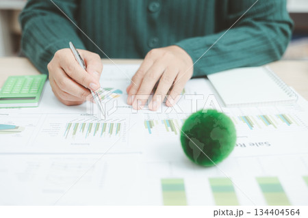 Eco-friendly business concept with hand analyzing financial charts and green earth globe symbolizing sustainable investment, environmental data analysis and green economy growth. green business. Eco-friendly business concept with hand analyzing financial charts and green earth globe symbolizing sustainable investment, environmental data analysis and green economy growth. green business. 134404564