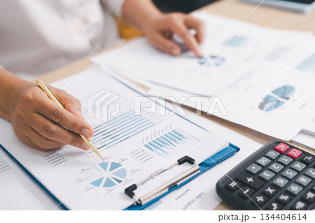 Close up of businessperson analyzing financial chart and graph with pen and calculator on desk, concept of accounting management, budget planning, financial report and data analysis. Close up of businessperson analyzing financial chart and graph with pen and calculator on desk, concept of accounting management, budget planning, financial report and data analysis. 134404614