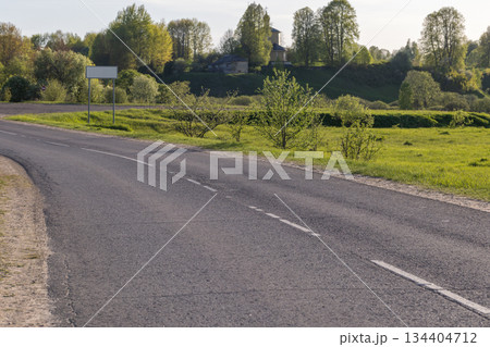A quiet rural road winds through lush green fields under a sunny sky 134404712
