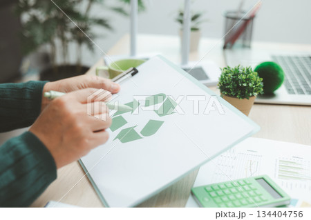 Business person holding recycle symbol on clipboard with green charts on desk, representing circular economy, eco responsibility, sustainability and environmental business concept. 134404756