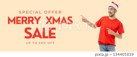 Young man in casual red shirt and Santa hat points at sale sign 134405839