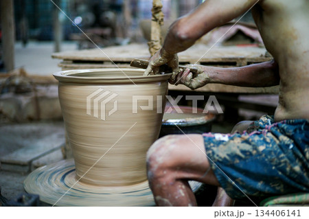 The skilled worker doing the clay work on the spinning wheel for modeling the shape of jar. The skilled worker doing the clay work on the spinning wheel for modeling the shape of jar. 134406141