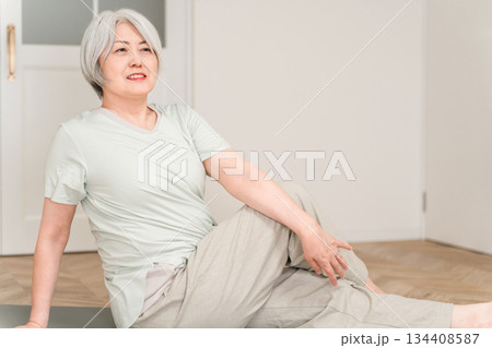 部屋でヨガマットを引いてストレッチ,柔軟体操するグレイヘアーのシニア女性 部屋でヨガマットを引いてストレッチ,柔軟体操するグレイヘアーのシニア女性 134408587