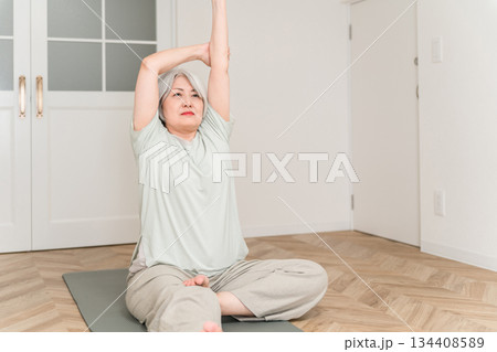 部屋でヨガマットを引いてストレッチ,柔軟体操するグレイヘアーのシニア女性 部屋でヨガマットを引いてストレッチ,柔軟体操するグレイヘアーのシニア女性 134408589