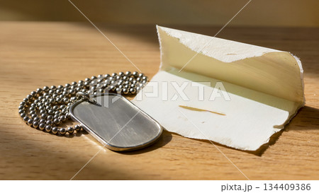Military dog tag and an old letter on a wooden table in the morning light. 134409386