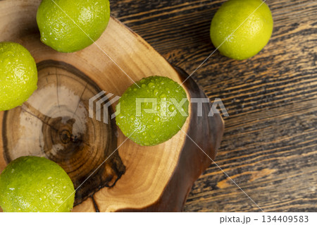wet green ripe citrus limes scattered on the wooden table in the kitchen, juicy lime fruits for cooking, green limes covered with drops of water 134409583