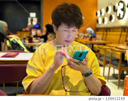Woman using mobile phone at cafe. Focused attention, modern lifestyle, casual dining experience, social interaction. 134411159