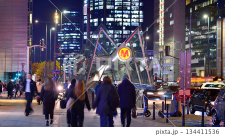 Warsaw, Poland. 4 November 2025. Entrance to the subway in center city in the night. People go to the subway. Lights street and buildings towering around them. Nearby with cars passing. 134411536