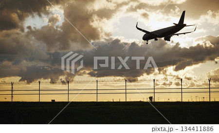Passenger airplane landing at sunset behind airport fence with barbed wire 134411886