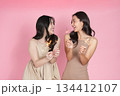 Festive moment. Two young women holding sparklers and smiling against a pink backdrop. 134412107