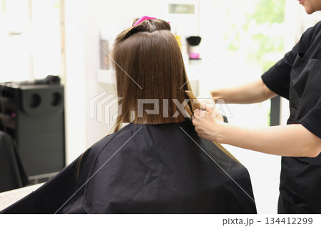 Unrecognisable hairdresser cutting female client hair with professional barber scissors and comb and making stylish haircut short bob hairstyle in beauty salon. Hair care, hair salon and hairstyling 134412299