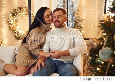 In love, sitting on the sofa. Couple is celebrating new year indoors together 134412451