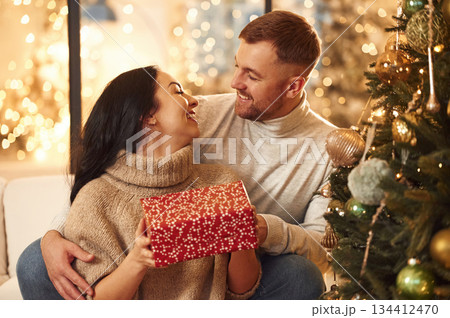With red gift box, sharing love. Couple is celebrating new year indoors together With red gift box, sharing love. Couple is celebrating new year indoors together 134412470