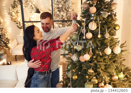 They decorate the Christmas tree. Couple is celebrating new year indoors together They decorate the Christmas tree. Couple is celebrating new year indoors together 134412603