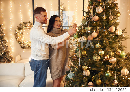 Decorating the Christmas tree. Couple is celebrating new year indoors together 134412622