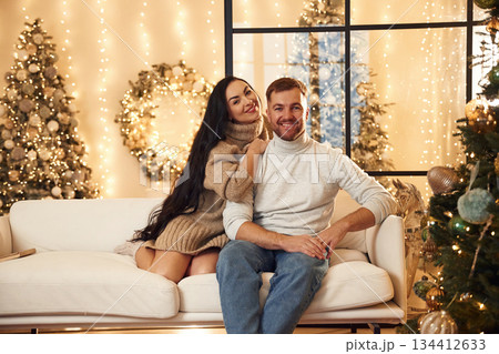 Sitting and smiling. Couple is celebrating new year indoors together Sitting and smiling. Couple is celebrating new year indoors together 134412633