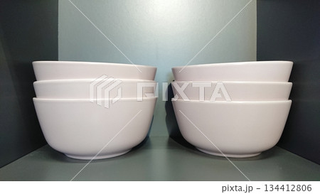 Stacked white ceramic bowls on shelf 134412806
