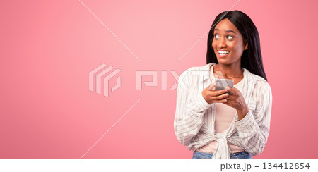 Millennial black woman with cellphone looking aside at empty space, pink studio background. Happy African American lady using mobile device, communicating online, putting out post in social media Millennial black woman with cellphone looking aside at empty space, pink studio background. Happy African American lady using mobile device, communicating online, putting out post in social media 134412854