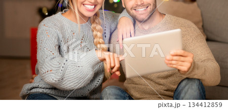 Loving couple having fun together at home on xmas, sitting on floor by couch and using digital tablet, copy space. Emotional young man and woman playing game online on pad together Loving couple having fun together at home on xmas, sitting on floor by couch and using digital tablet, copy space. Emotional young man and woman playing game online on pad together 134412859