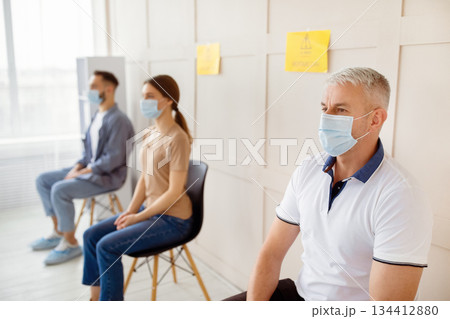 Covid-19 vaccination. Senior man in face mask waiting to receive coronavirus vaccine injection, sitting in queue at clinic, free space. Population immunization campaign, viral disease prevention 134412880