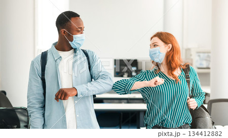 New Normal. Diverse multiethnic students doing elbow bumping standing together at classroom, wearing single-use surgical masks and backpack. Black guy and red-haired woman avoid coronavirus spread New Normal. Diverse multiethnic students doing elbow bumping standing together at classroom, wearing single-use surgical masks and backpack. Black guy and red-haired woman avoid coronavirus spread 134412882