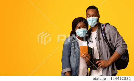Coronavirus And Tourism. Portrait Of African American Couple In Medical Masks With Passports In Hands Ready For Vacation During Pandemic, Standing Isolated Over Yellow Studio Background, Copy Space Coronavirus And Tourism. Portrait Of African American Couple In Medical Masks With Passports In Hands Ready For Vacation During Pandemic, Standing Isolated Over Yellow Studio Background, Copy Space 134412886