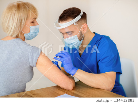 Covid-19 vaccination for senior people. Mature woman receiving coronavirus vaccine injection at clinic. Doctor in face mask administering shot to elderly patient. Preventive measures against virus 134412893