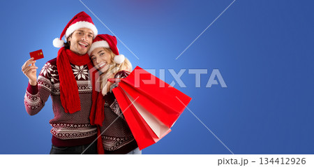 Christmas gifts. Romantic girl and her boyfriend with shopping bags and credit card on blue background, free space 134412926