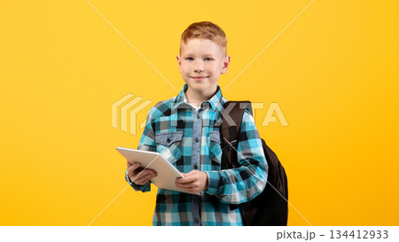 Technologies in school education. Smiling smart schoolboy with backpack holding digital tablet over yellow studio background, copy space. Cute kid using pad for studying, doing homework, websurfing Technologies in school education. Smiling smart schoolboy with backpack holding digital tablet over yellow studio background, copy space. Cute kid using pad for studying, doing homework, websurfing 134412933