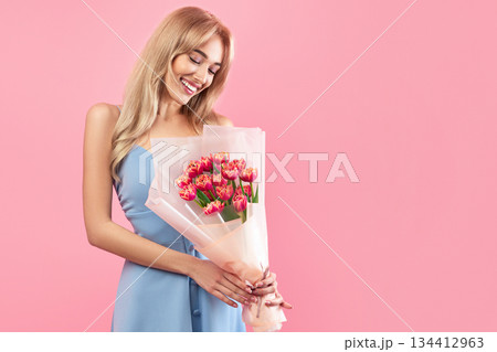 Positive young lady holding lovely tulips on pink studio background. Charming millennial blonde model with bunch of flowers for Woman's Day. Fun spring holiday concept Positive young lady holding lovely tulips on pink studio background. Charming millennial blonde model with bunch of flowers for Woman's Day. Fun spring holiday concept 134412963