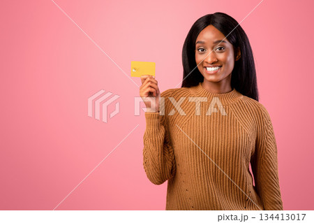 Portrait of satisfied female client showing credit card on pink studio background. Happy African American woman recommending bank services, smiling and looking at camera Portrait of satisfied female client showing credit card on pink studio background. Happy African American woman recommending bank services, smiling and looking at camera 134413017