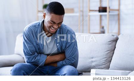 Food Poisoning. Black Man Suffering From Stomachache After Eating Pizza Touching Aching Abdomen Sitting On Couch At Home. Health Problem, Appendicitis, Abdominal Inflammation And Gastritis Concept. Food Poisoning. Black Man Suffering From Stomachache After Eating Pizza Touching Aching Abdomen Sitting On Couch At Home. Health Problem, Appendicitis, Abdominal Inflammation And Gastritis Concept. 134413126