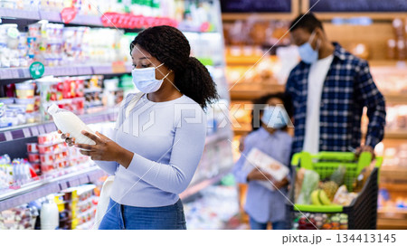 Young black woman with her family purchasing dairy products at modern supermarket during covid quarantine, copy space. Millennial consumers shopping for food at huge mall Young black woman with her family purchasing dairy products at modern supermarket during covid quarantine, copy space. Millennial consumers shopping for food at huge mall 134413145