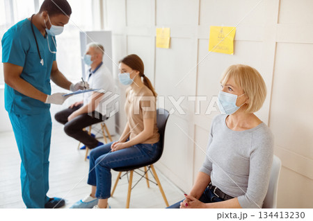 Male doctor talking to young woman, taking notes before covid-19 vaccine injection at clinic waiting room. Coronavirus immunization, protection against global virus campaign 134413230