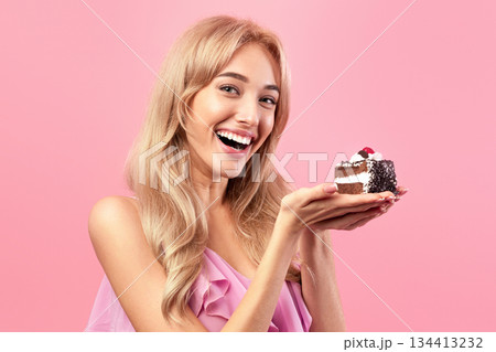 Pretty Caucasian woman holding yummy cake, smiling and looking at camera on pink studio background. Beautiful blonde woman celebrating birthday, enjoying delicious dessert Pretty Caucasian woman holding yummy cake, smiling and looking at camera on pink studio background. Beautiful blonde woman celebrating birthday, enjoying delicious dessert 134413232