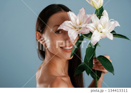 Holding lily flower. Young woman is in the studio against background Holding lily flower. Young woman is in the studio against background 134413311