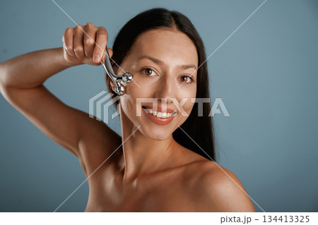 Skin massager. Young woman is in the studio against background Skin massager. Young woman is in the studio against background 134413325