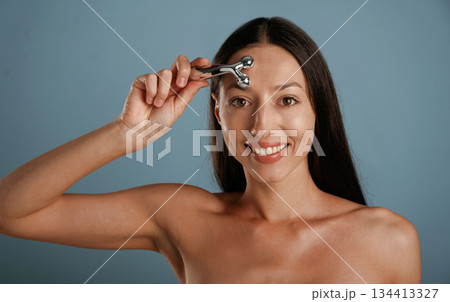Skin massager. Young woman is in the studio against background 134413327