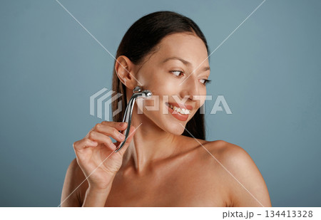 Skin massager. Young woman is in the studio against background Skin massager. Young woman is in the studio against background 134413328