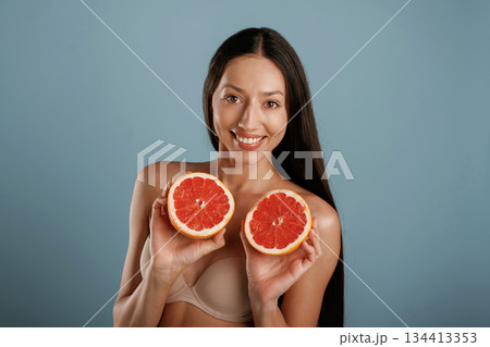 Grapefruit, conception of healthy eating. Young woman is in the studio against background Grapefruit, conception of healthy eating. Young woman is in the studio against background 134413353