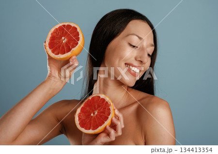 Grapefruit, conception of healthy eating. Young woman is in the studio against background Grapefruit, conception of healthy eating. Young woman is in the studio against background 134413354