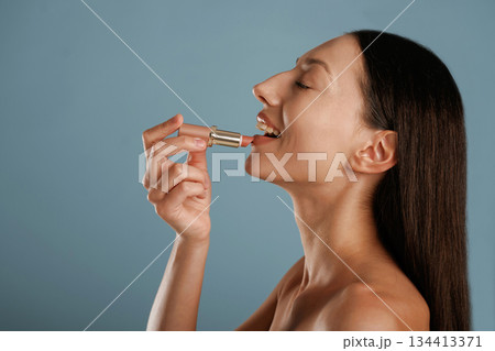 Applying lipstick. Young woman is in the studio against background 134413371