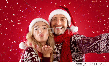 Affectionate millennial couple in Christmas clothes taking selfie together on red background Affectionate millennial couple in Christmas clothes taking selfie together on red background 134413422